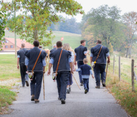 Hommes en costume traditionnel sur un chemin bordé de clôtures lors de la désalpe