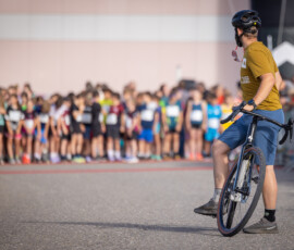 Bénévole à vélo devant la ligne de départ de la Course à travers Sâles 2026, en Gruyère